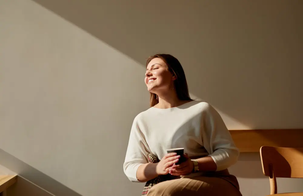 Woman smiling in sunlight holding a beverage.
